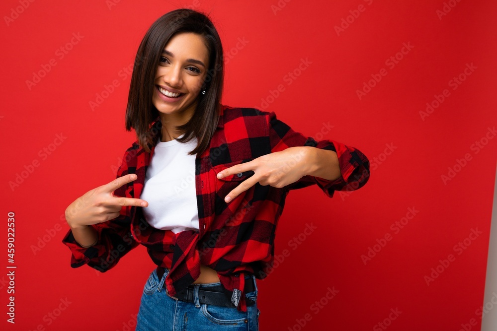 Young happy positive cool pretty brunette woman with sincere emotions wearing white t-shirt and trendy red check shirt isolated on red background with free space and having fun Young happy positive cool pretty brunette woman with sincere emotions wearing white t-shirt and trendy red check shirt isolated on red background with free space and having fun