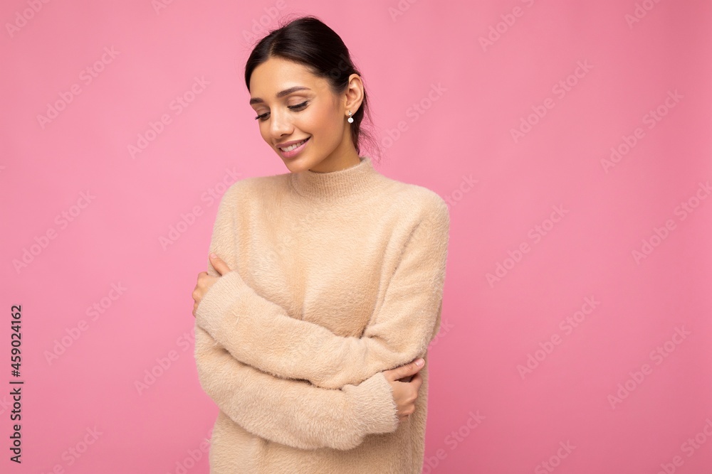 Portrait of beautiful positive cheerful cute smiling young brunette woman in casual beige sweater isolated on pink background with copy space Portrait of beautiful positive cheerful cute smiling young brunette woman in casual beige sweater isolated on pink background with copy space