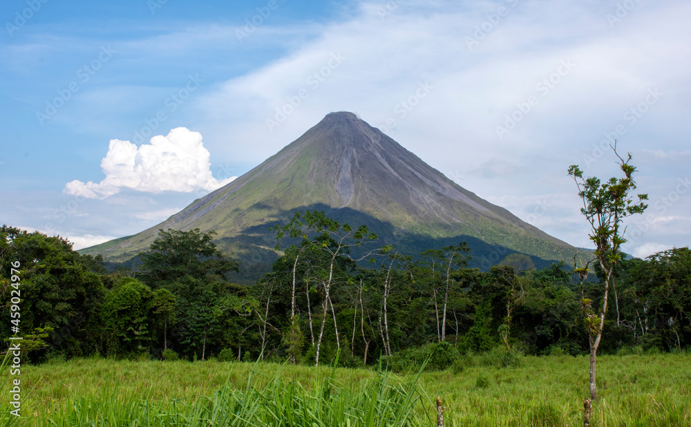 Volcano Arenal near tourist town of La Fortuna in Costa Rica. Cone-shaped volcano surrounded by jungle trees and cattle pasture. Volcano Arenal near tourist town of La Fortuna in Costa Rica. Cone-shaped volcano surrounded by jungle trees and cattle pasture.