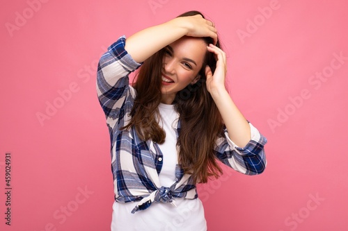 Photo portrait of young beautiful smiling hipster brunette woman in trendy blue and white shirt. Sexy carefree female person posing isolated near pink wall with empty space in studio. Positive model