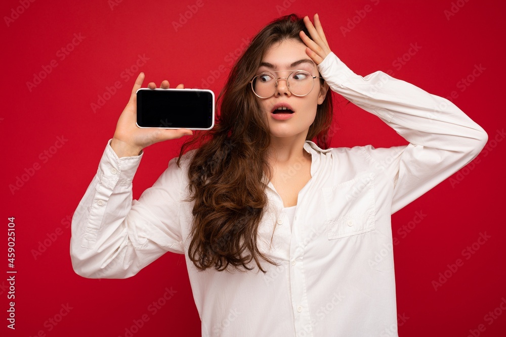 Naklejka premium Photo of beautiful shocked young woman good looking wearing casual stylish outfit standing isolated on background with copy space holding smartphone showing phone in hand with empty screen display for