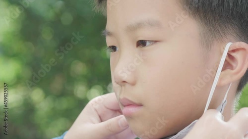 4k Selective focus young Asian boy with getting help to wear face mask to protect visus, on green background