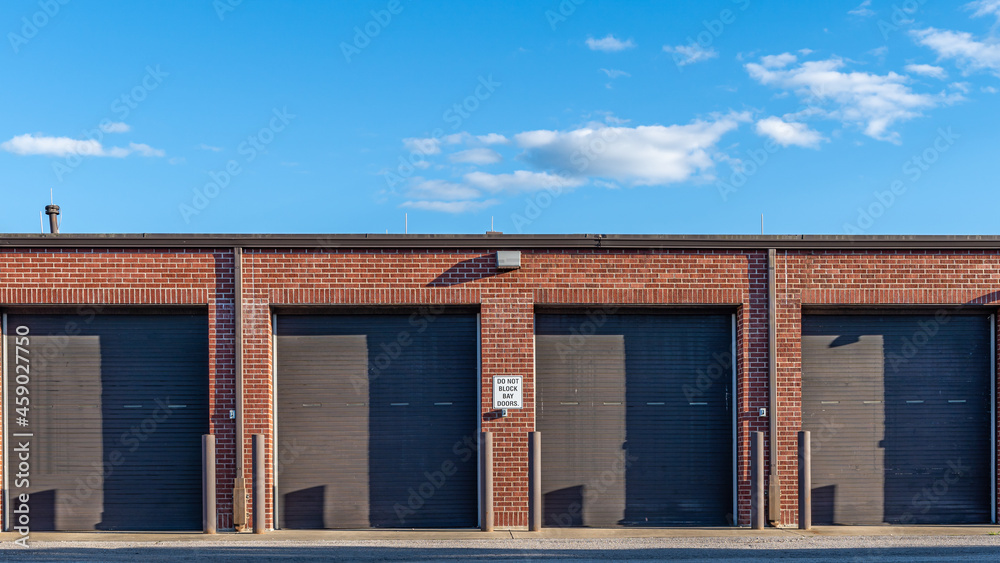 Maintenance bay garage doors on a brick building.  The sky above is an a sunny day with some white cumulus clouds visible.