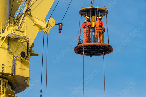 A group of workers consist of riggers and engineers riding a personal transfer basket, transferring from a tug boat to heavy lift pipelay barge at offshore oil field