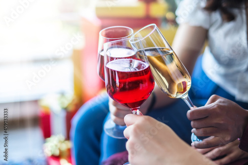 Women's hand holding glasses of red and white wine and clinking glasses in the Christmas party