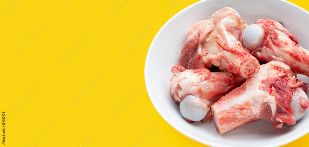 Raw pork bones in white bowl on yellow background.