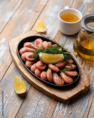 Cast iron pan filled with pink prawns with spices and lemon, top view on a wooden table