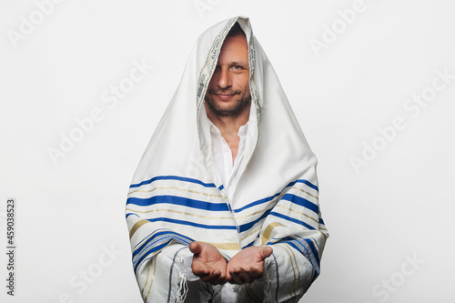A religious Jew wrapped in a Tallit, prayer shawl with the inscription "Baruch Atah Adonai" written on it in Hebrew with hands palms together receiving or giving gesture. Jewish Friday morning prayer