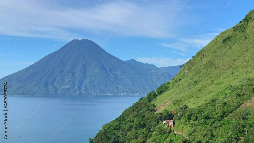 Central American volcano Volcan San Pedro in Lake Atitlan, Guatemala on a blue sunny day with boat traffic riding over the blue lake water and Santa Cruz La Laguna green hillside in the foreground. Central American volcano Volcan San Pedro in Lake Atitlan, Guatemala on a blue sunny day with boat traffic riding over the blue lake water and Santa Cruz La Laguna green hillside in the foreground.