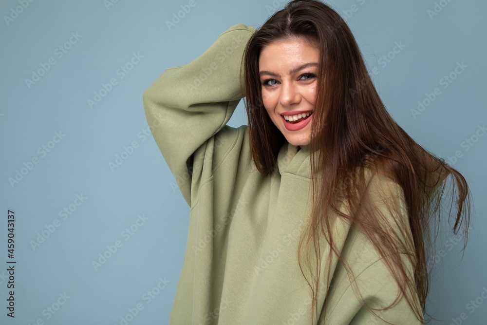 Portrait of young beautiful smiling girl in stylish hipster green hoodie. Sexy carefree woman posing near blue wall. Positive model having fun Portrait of young beautiful smiling girl in stylish hipster green hoodie. Sexy carefree woman posing near blue wall. Positive model having fun