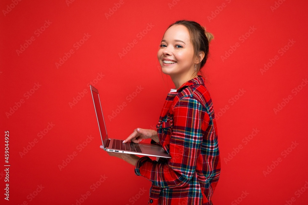 Photo of beautiful young girl holding computer laptop looking at camera isolated over colourful background Photo of beautiful young girl holding computer laptop looking at camera isolated over colourful background