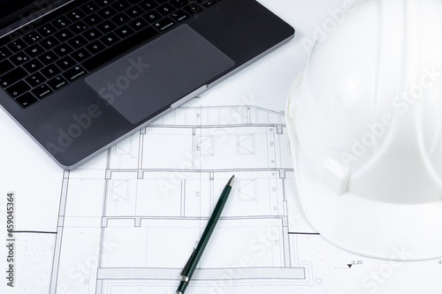 A pen, a white safety helmet and a laptop on the architectural plan. Engineering, architecture, contractor, construction background photo.