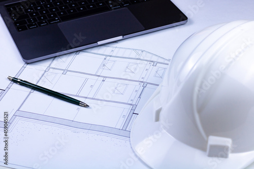 A pen, a white safety helmet and a laptop on the architectural plan. Engineering, architecture, contractor, construction background photo.