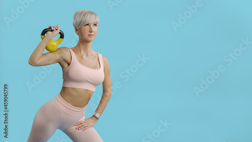 Beautiful athletic woman holding yellow kettlebell COPY SPACE BLUE BG photo