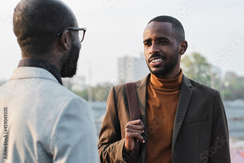 Horizontal over-the-shoulder shot of handsome young African American man standing in front of his co-worker discussing something during break
