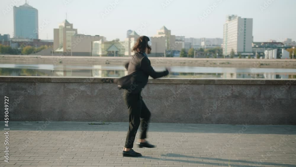 Looping of happy businessman walking outdoors jumping wearing headphones listening to music and expressing happiness. People and good mood concept. Looping of happy businessman walking outdoors jumping wearing headphones listening to music and expressing happiness. People and good mood concept.
