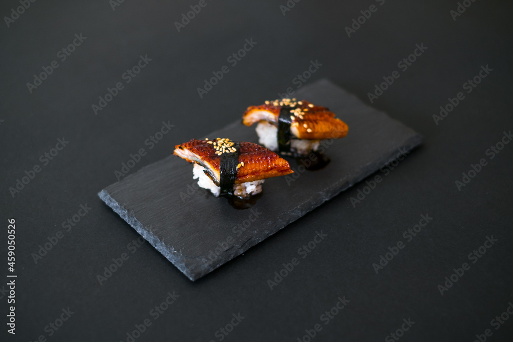 Japanese Sushi - Two Unagi Nigiri Sushi on black stone board. Sushi pieces served on black slate isolated on black background. Sushi with backed eel Japanese Sushi - Two Unagi Nigiri Sushi on black stone board. Sushi pieces served on black slate isolated on black background. Sushi with backed eel