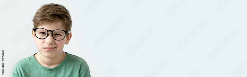 Fototapeta premium Surprised boy in a green T-shirt and glasses pensive scratches his head. Copy space.