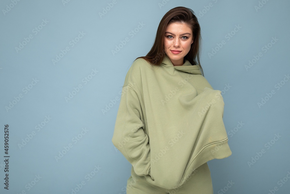 Photo of beautiful young brunette cool woman in a stylish khaki hoodie isolated on blue background. Mockup. Empty space Photo of beautiful young brunette cool woman in a stylish khaki hoodie isolated on blue background. Mockup. Empty space