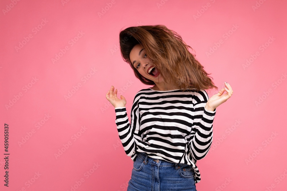 Young beautiful brunet woman. Trendy lady in casual striped longsleeve. Positive female shows facial sincere emotions. Funny model isolated on pink background with free space Young beautiful brunet woman. Trendy lady in casual striped longsleeve. Positive female shows facial sincere emotions. Funny model isolated on pink background with free space