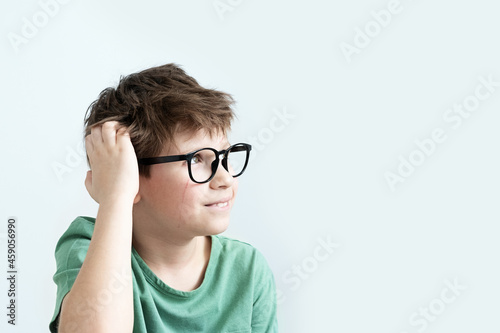 scratch boy in a green T-shirt and glasses pensive scratches his head. Copy space.
