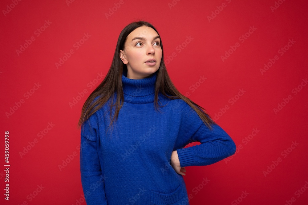 Young concentrated dreaming attractive brunette woman with sincere emotions isolated on background wall with copy space wearing casual trendy blue sweater. Thoughtful concept Young concentrated dreaming attractive brunette woman with sincere emotions isolated on background wall with copy space wearing casual trendy blue sweater. Thoughtful concept