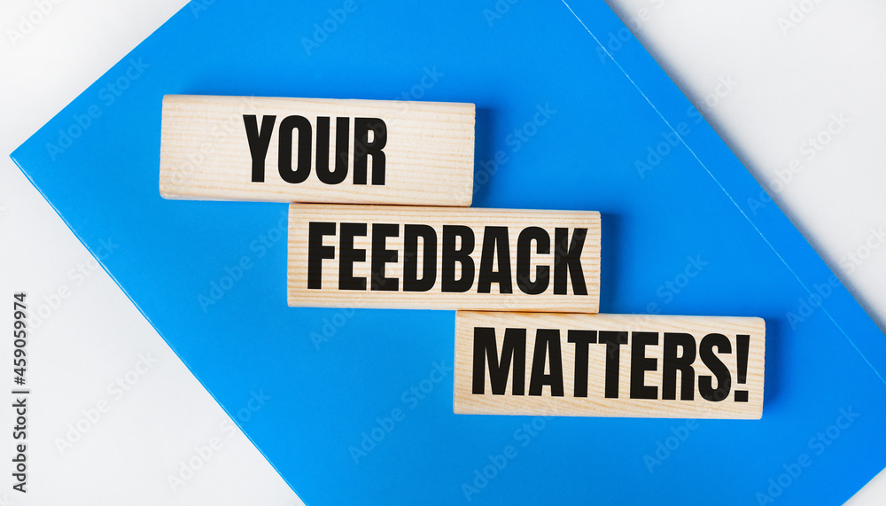 There is a blue notebook on a light gray background. Above are three wooden blocks with the words YOUR FEEDBACK MATTERS There is a blue notebook on a light gray background. Above are three wooden blocks with the words YOUR FEEDBACK MATTERS