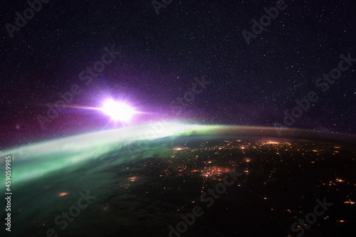 Fototapeta Naklejka Na Ścianę i Meble -  Night planet earth with amazing green polar lights and purple starry space with a bright star. Bright city lights of megacities, view from space