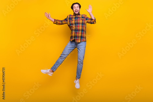 Full length photo of funny brunet millennial guy jump wear shirt jeans sneakers isolated on yellow background