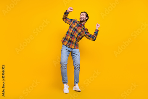 Full size photo of funny brunet millennial guy dance look wear shirt jeans sneakers isolated on yellow background