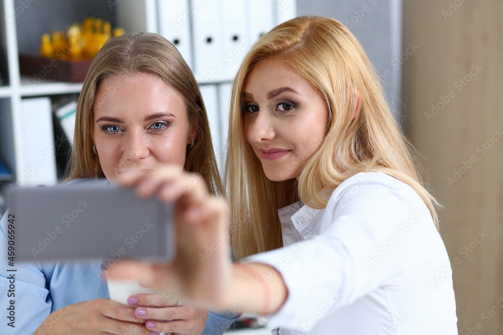 Two businesswomen in the office smile and do selfie Two businesswomen in the office smile and do selfie