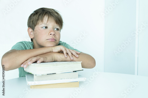 Sad boy with book does school homework. Back to school. Unhappy schoolboy with textbooks. Distance learnin photo