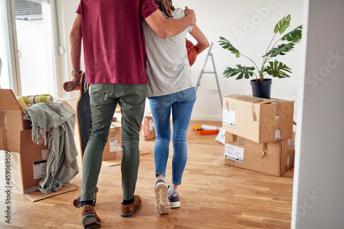 cropped image from behind of young male hugging his female partner in new apartment, holding skateboard, while she caring basketball