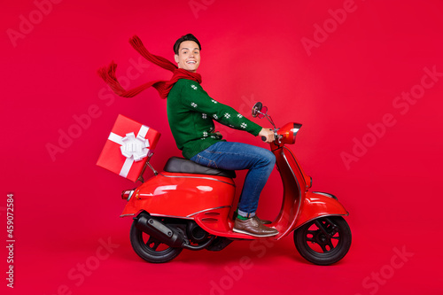 Full length body size photo smiling guy sitting on bike in scarf driving scooter isolated vibrant red color background