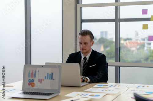 smart handsome Caucasian businessman focus on working with laptop on meeting desk in modern office with confidence. tablet computer with graphs, diagrams and charts on screen. financial analysis.