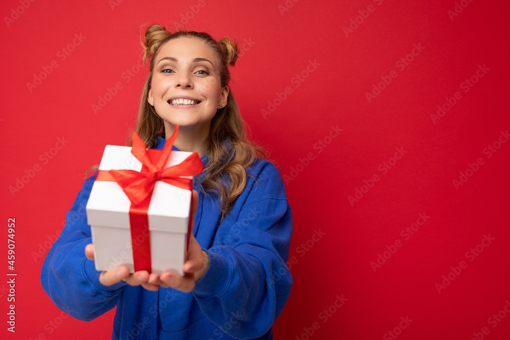 Shot of attractive positive smiling young blonde woman isolated over colourful background wall wearing everyday trendy outfit holding gift box and looking at camera Shot of attractive positive smiling young blonde woman isolated over colourful background wall wearing everyday trendy outfit holding gift box and looking at camera