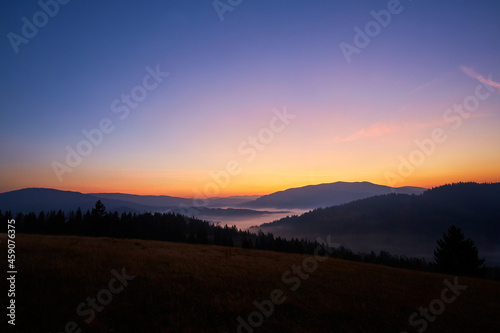 Nice autumn sunrise in the mountains. The sun hid behind the mountain. The fog lies in the low