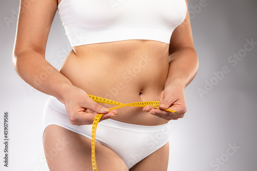 Woman measuring waist on gray background
 photo