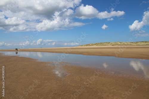 Landscape of beautiful sandy beach with no people and sands stretched to horizon with white puffy clouds reflected in the water pools in Holkham north Norfolk East Anglia uk