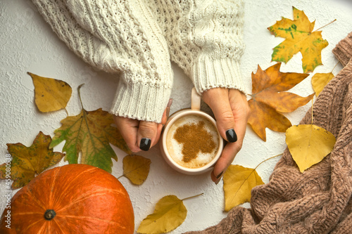 Woman hands holding morning cup of coffee decorated autumn yellow leaves
