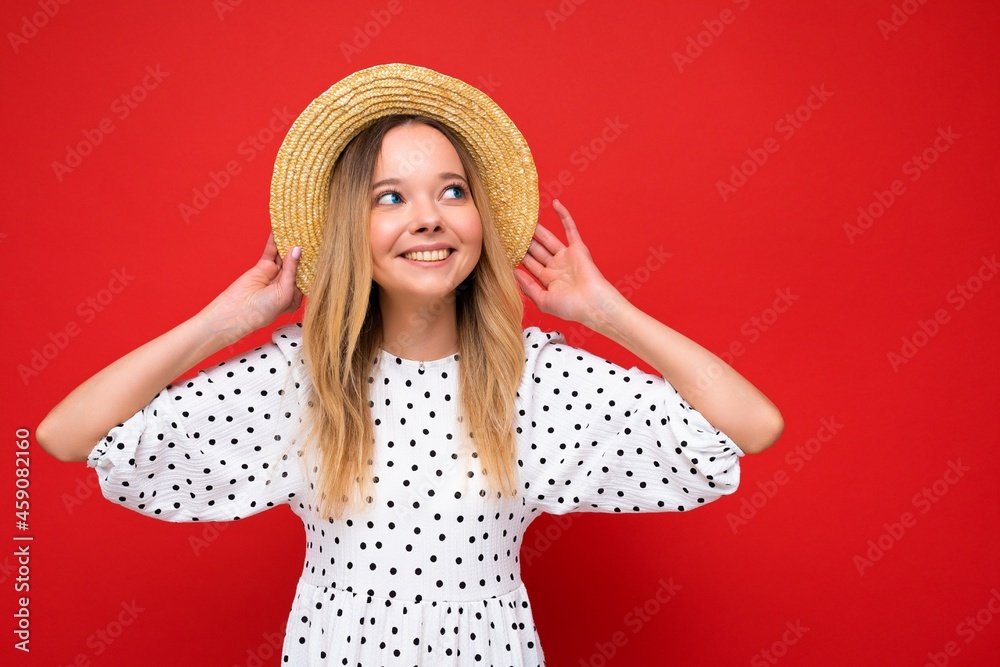 Young beautiful woman. Trendy woman in casual summer dress and straw hat. Positive female shows facial emotions. Funny model isolated on red background Young beautiful woman. Trendy woman in casual summer dress and straw hat. Positive female shows facial emotions. Funny model isolated on red background