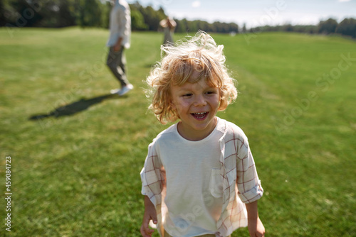 Portrait of adorable little boy smiling away while playing catch together with his parents in green park on a summer day