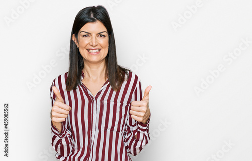 Beautiful brunette woman wearing striped shirt success sign doing positive gesture with hand, thumbs up smiling and happy. cheerful expression and winner gesture.