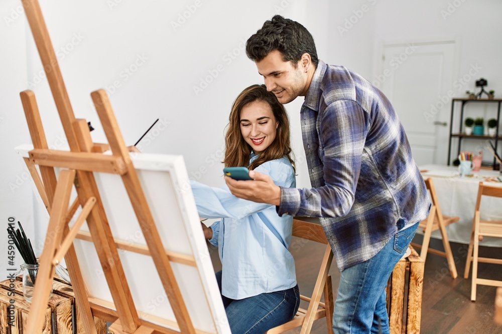 Two hispanic students smiling happy painting and using smartphone at art school. Two hispanic students smiling happy painting and using smartphone at art school.