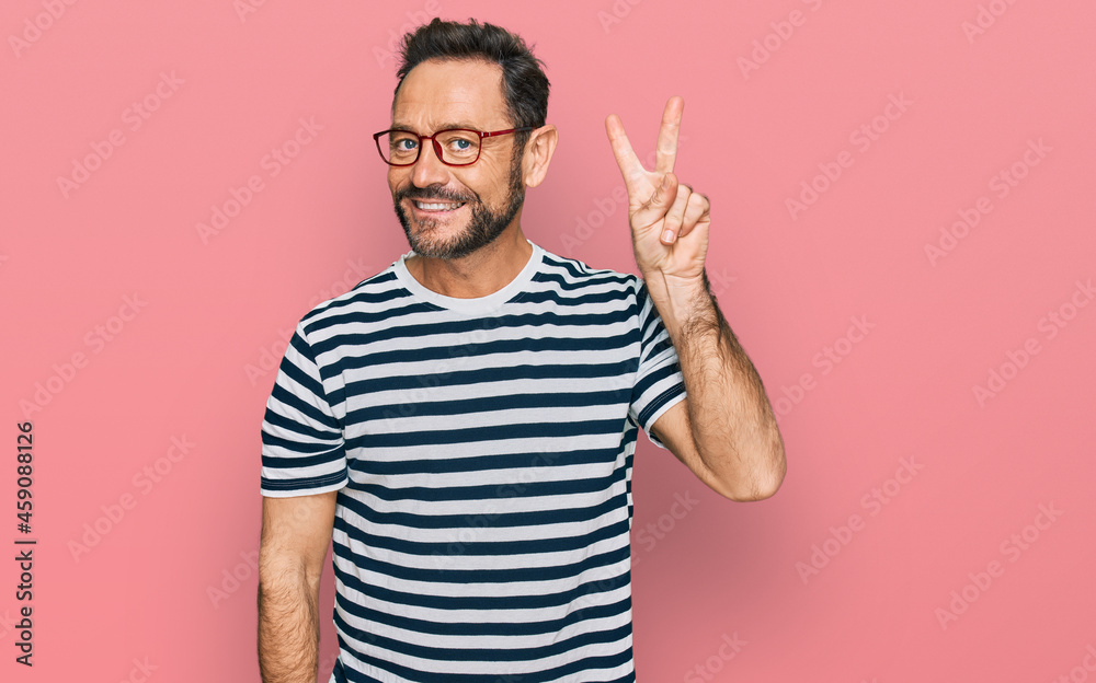 Middle age man wearing casual clothes and glasses showing and pointing up with fingers number two while smiling confident and happy. Middle age man wearing casual clothes and glasses showing and pointing up with fingers number two while smiling confident and happy.