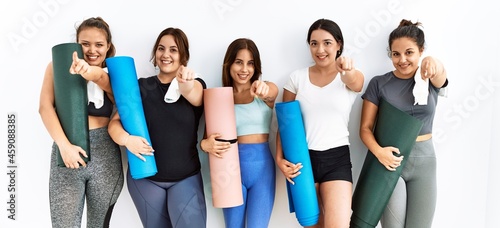 Group of women holding yoga mat standing over isolated background pointing to you and the camera with fingers, smiling positive and cheerful