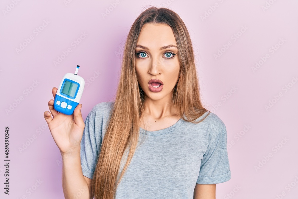 Young blonde girl holding glucometer device scared and amazed with open mouth for surprise, disbelief face Young blonde girl holding glucometer device scared and amazed with open mouth for surprise, disbelief face