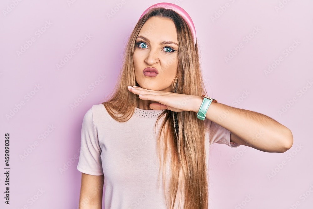 Young blonde girl wearing casual clothes cutting throat with hand as knife, threaten aggression with furious violence Young blonde girl wearing casual clothes cutting throat with hand as knife, threaten aggression with furious violence