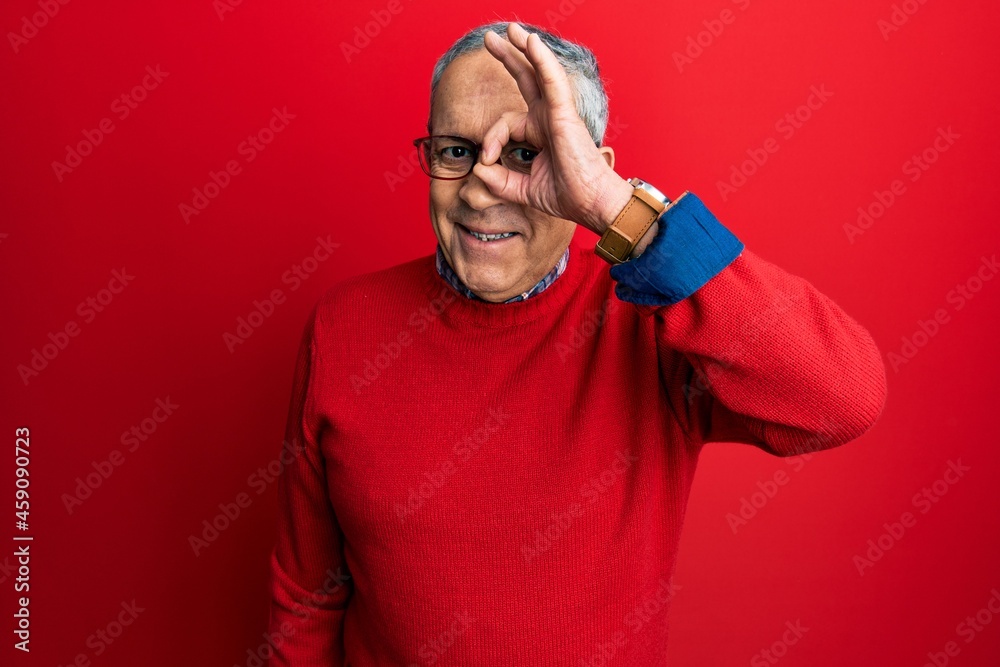 Handsome senior man with grey hair wearing casual clothes and glasses doing ok gesture with hand smiling, eye looking through fingers with happy face.