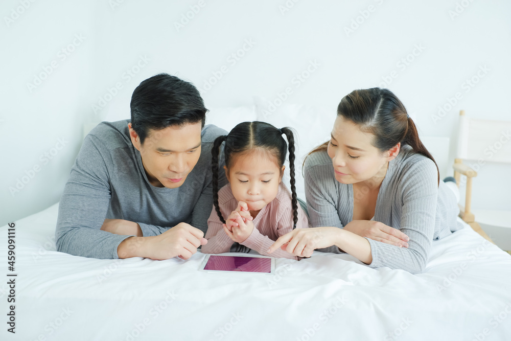Asian family playing tablet together on the bed in bedroom Asian family playing tablet together on the bed in bedroom